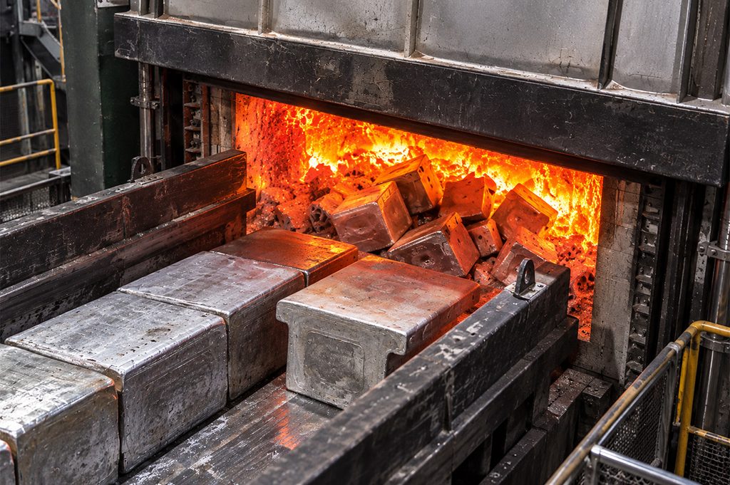 KI-generiert: Industrieofen mit gluehenden Metallbloecken in leuchtendem Orange und Grau